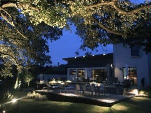 A modern home's backyard is visible at night by outdoor lighting
