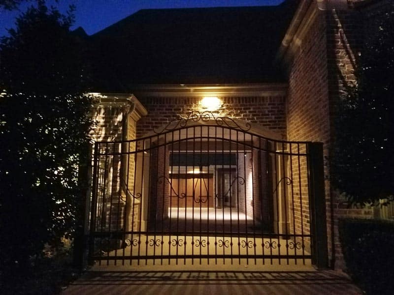 A porch with a soffit security light and a wrought iron fence in front of it