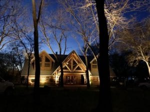 a cabin in the wood lit up with exterior lighting