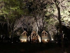 a cabin in the wood lit up with exterior lighting