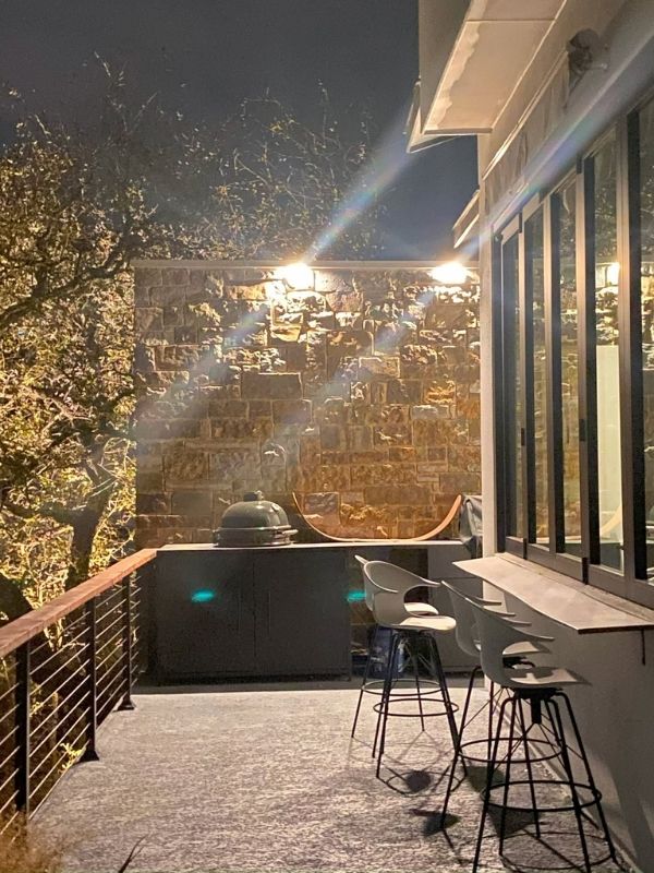 A patio with an outdoor kitchen that is lit with task and overhead lighting.