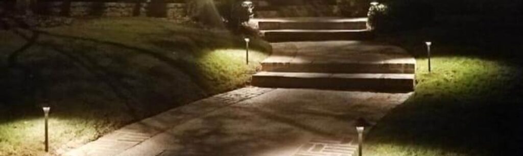 Nighttime garden pathway with four small lights along edges leading to stone steps